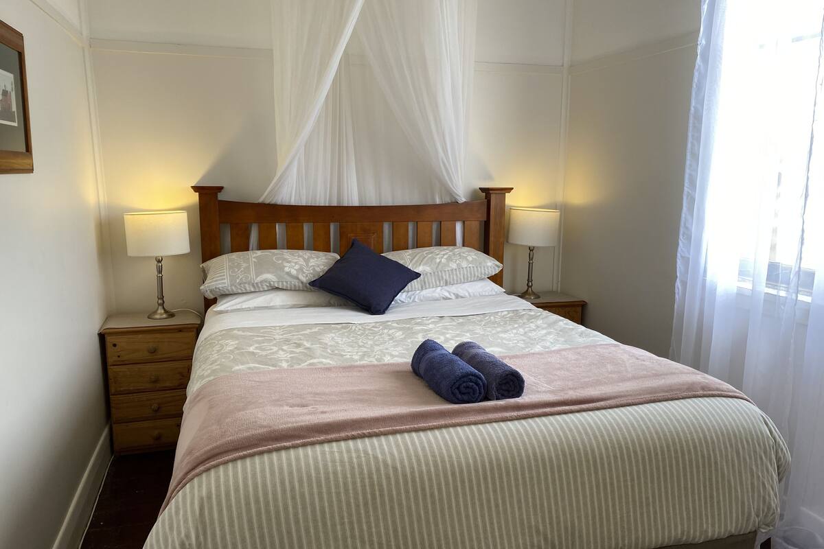 Una cama bien hecha con dosel, dos lámparas de noche y una mesita de madera.