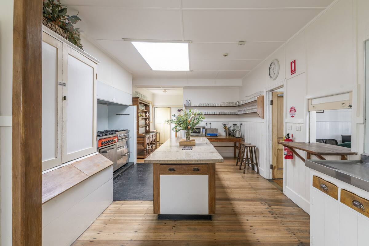 Una cocina con suelo de madera, una isla central, armarios blancos y un reloj en la pared.