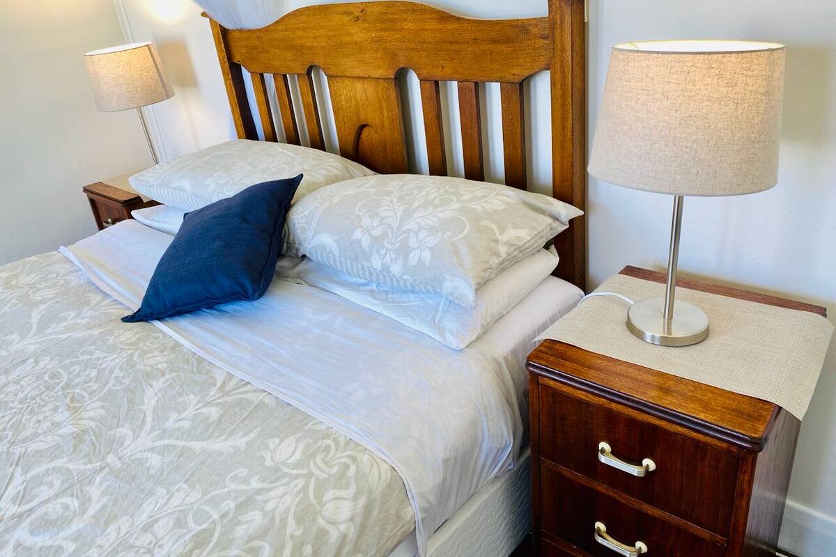 Una cama bien hecha con un cabecero de madera, dos mesitas de noche con lámparas y una cómoda con cajones.