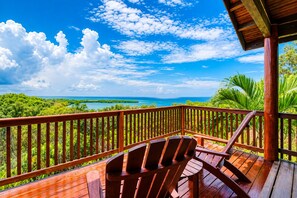 Une terrasse en bois, agrémentée de chaises, offre une vue imprenable sur un paysage tropical et l’océan.