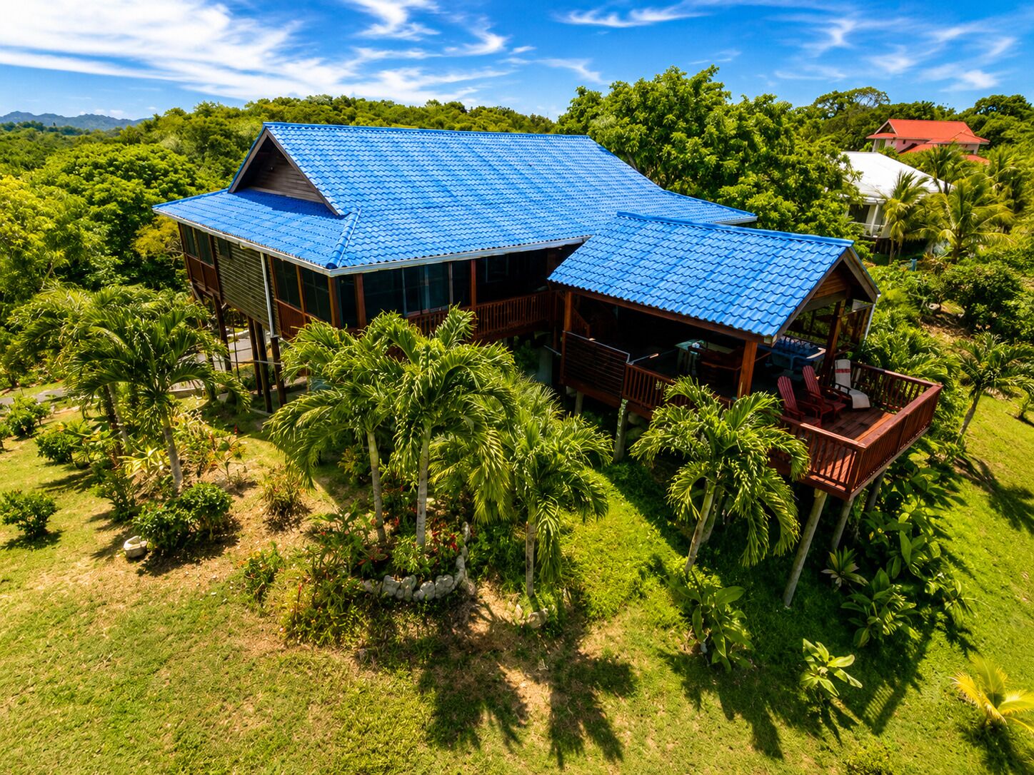 A large house with a blue roof, surrounded by lush greenery and palm trees.