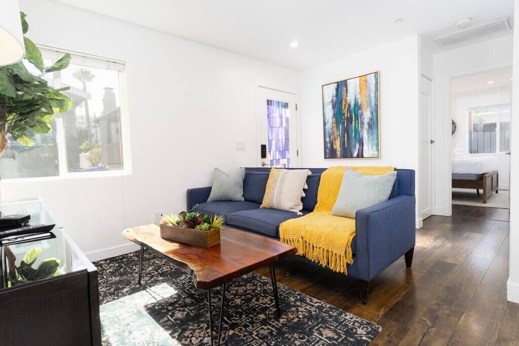 A modern living room with a blue sofa, a wooden coffee table, and a large abstract painting on the wall.