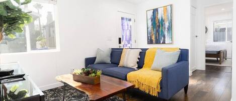 A modern living room with a blue sofa, a wooden coffee table, and a large abstract painting on the wall.