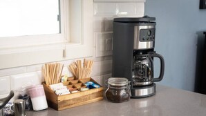 A kitchen counter with a coffee maker, a jar of sugar, a wooden box with utensils, and a glass jar of spices.