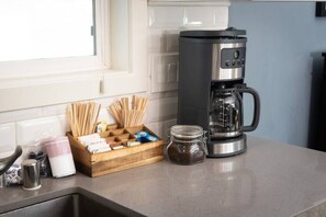 Eine Küchenarbeitsplatte mit einer Kaffeemaschine, einer Zuckerdose, einer Holzkiste mit Besteck und einem Glas mit Gewürzen.