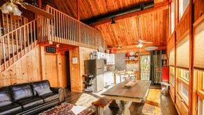 A wooden cabin interior with a sofa, dining table, and kitchen area.
