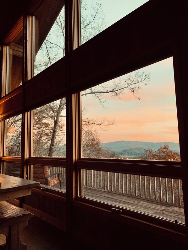 A room with large windows, a wooden bench, and a view of trees and hills.