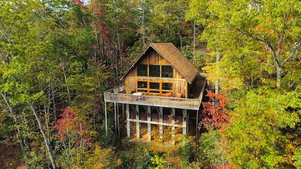 A wooden cabin with a balcony, surrounded by autumn foliage.