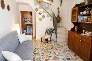 Un salon avec un canapé gris, un sol à motifs, une bibliothèque en bois et un escalier.