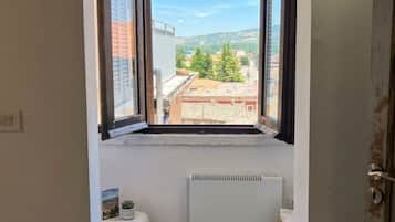 Une pièce avec une fenêtre donnant sur un paysage urbain, un radiateur situé sous la fenêtre et une porte sur le côté droit.
