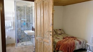 A bedroom with a bed, a wooden door, a shower area with a glass enclosure, and a white sink.