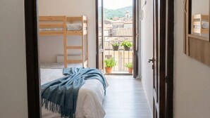 A bedroom with a bunk bed, a balcony with potted plants, and a view of buildings.