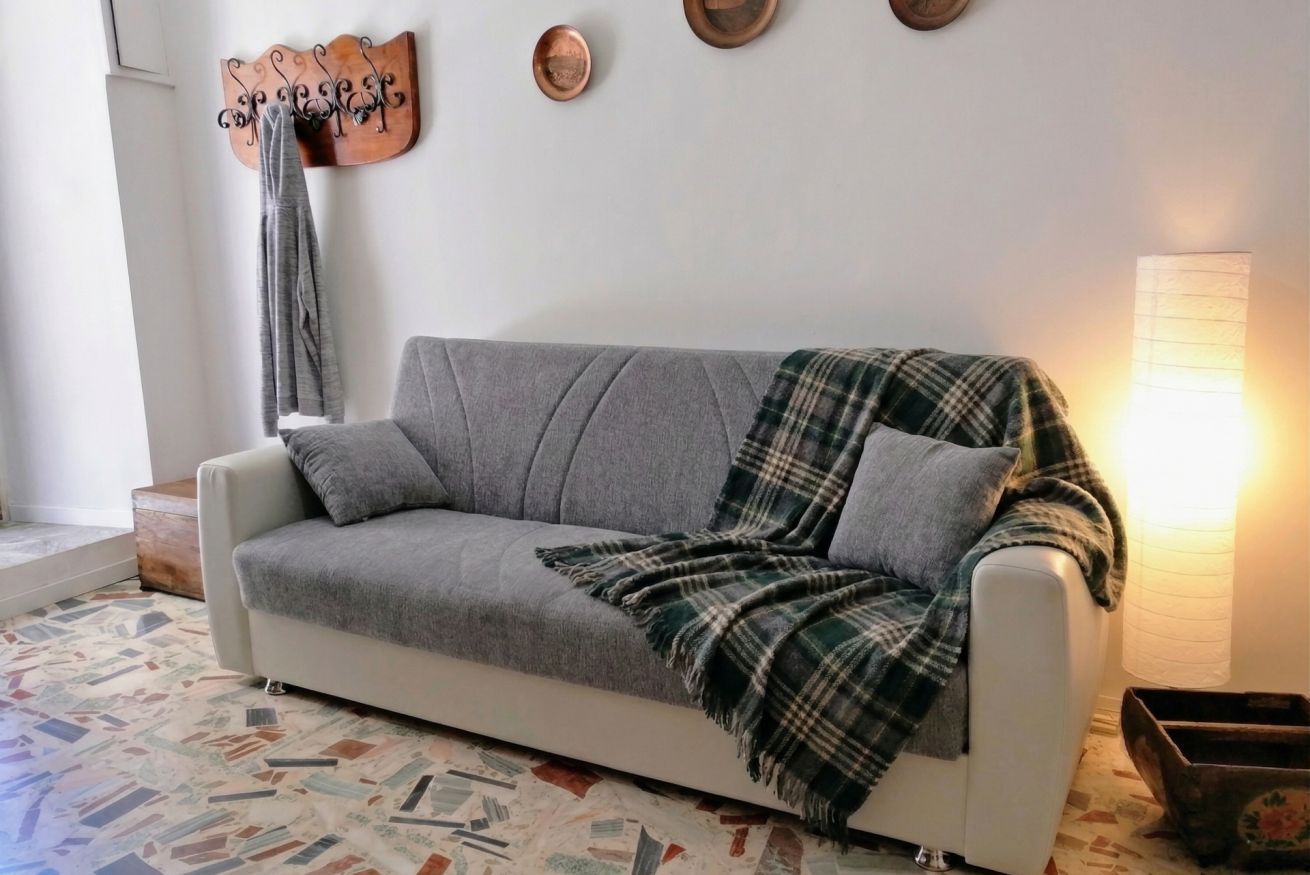 En grå soffa med en rutig pläd, en väggmonterad klädhängare och en golvlampa.