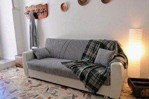 Un canapé gris avec une couverture à carreaux, un porte-manteau fixé au mur et une lampe sur pied.