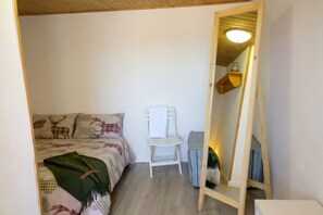 Une chambre à coucher avec un lit, une chaise, un miroir et une étagère sur laquelle se trouve un vase.