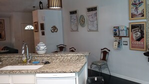 Una cocina con encimeras de granito, un refrigerador blanco, un lavamanos y un comedor con una silla y una pequeña mesa.