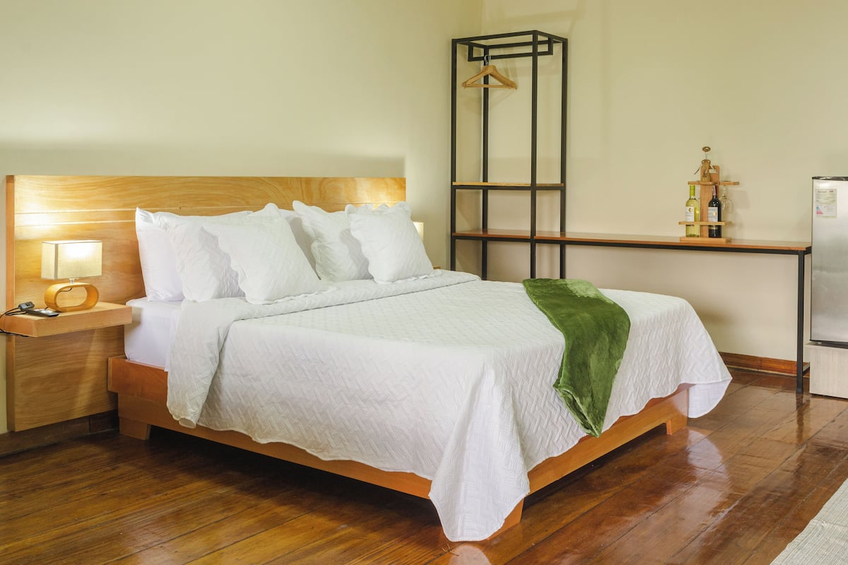 A neatly made bed with white linens, a bedside lamp, and a wooden nightstand.