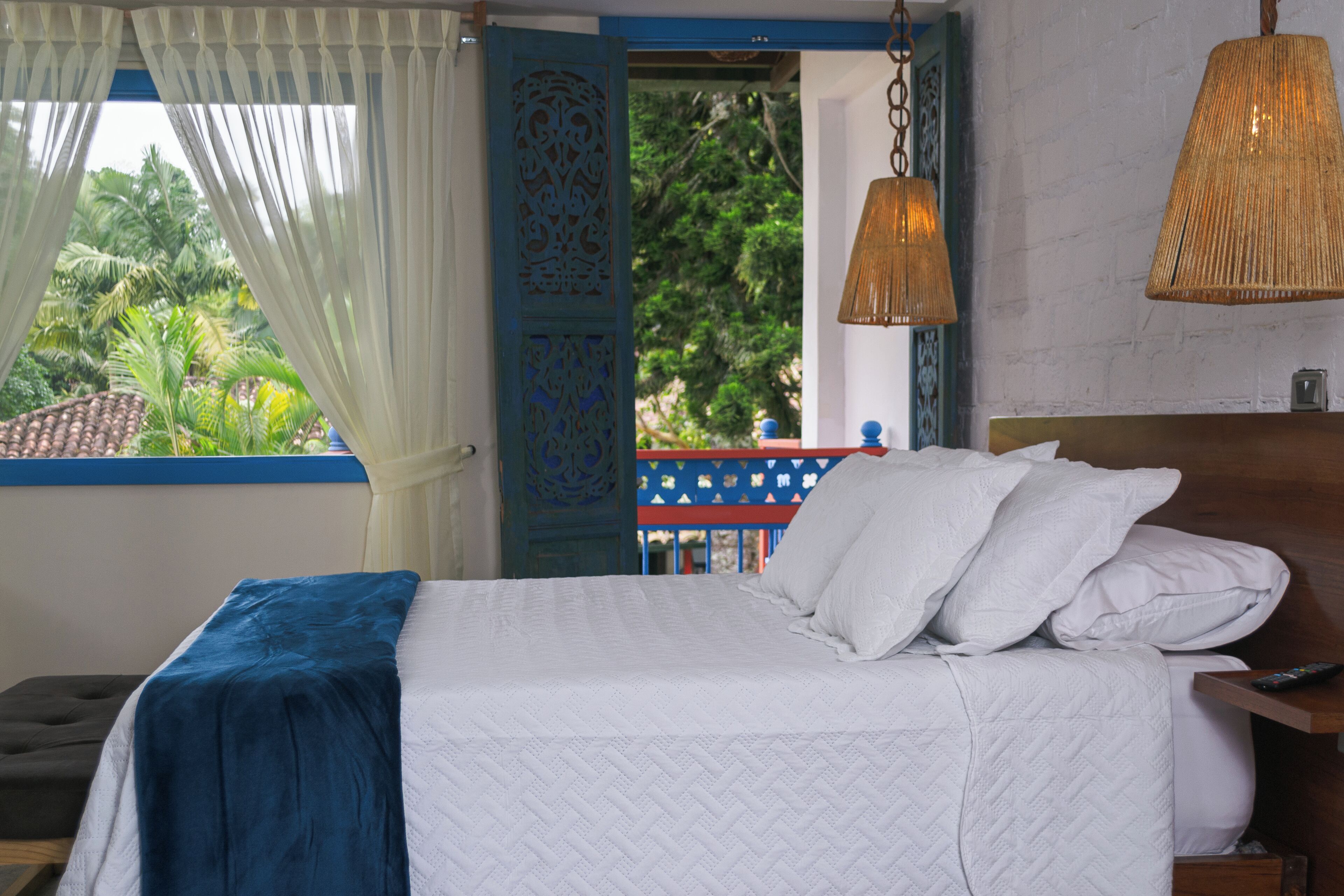 A bed with white bedding, a blue accent, and a remote control on a wooden nightstand.