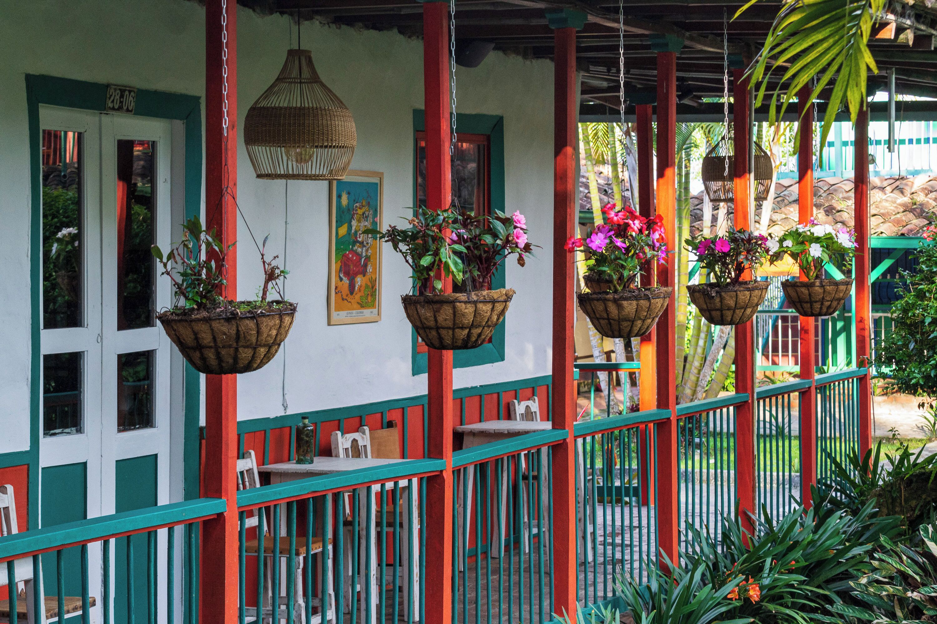A covered outdoor seating area with hanging planters and a red and green railing.