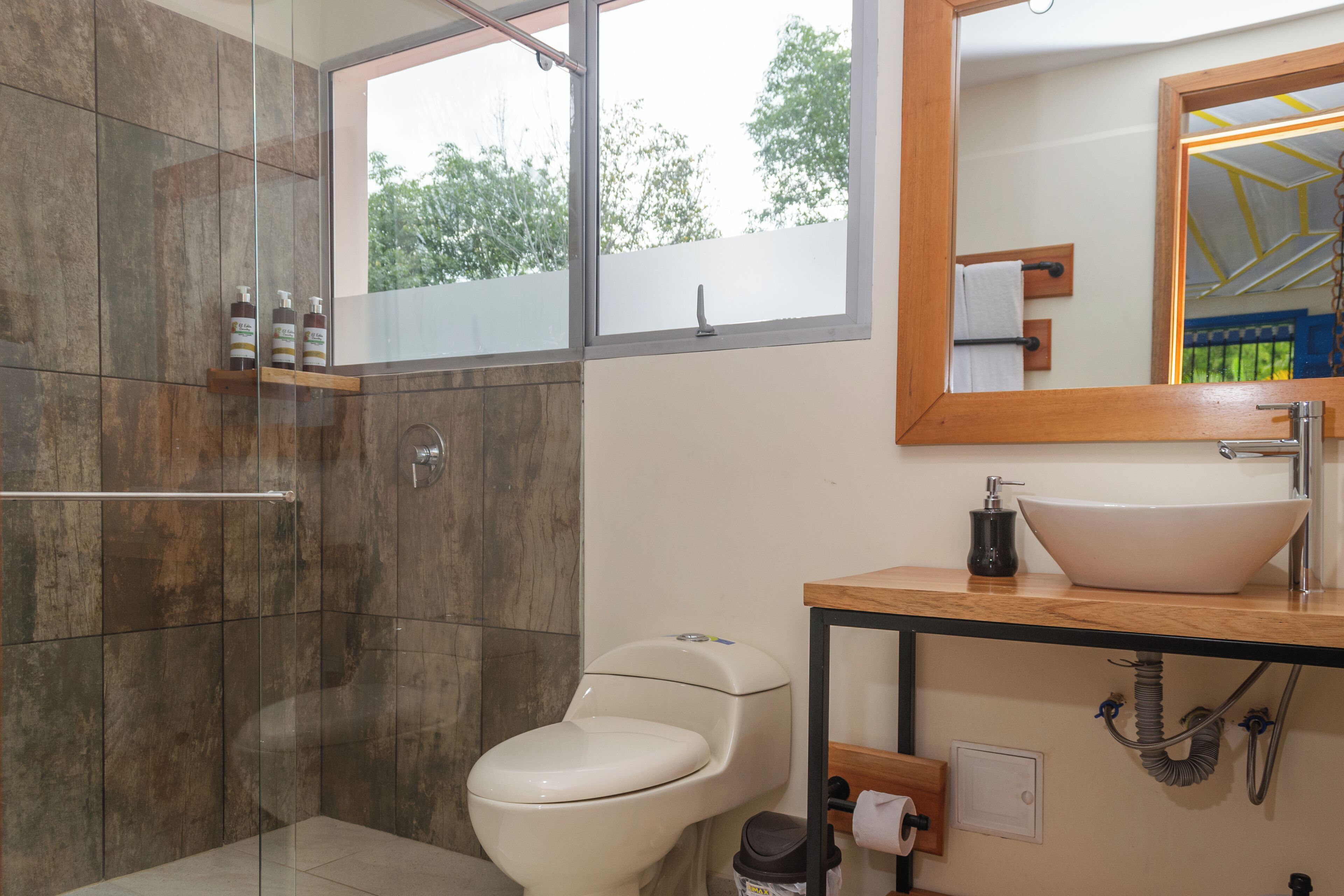 Une salle de bain moderne avec une douche à parois de verre, des toilettes blanches et un meuble-lavabo en bois doté d’un vasque sur pied.