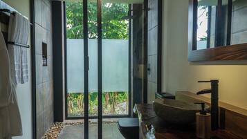 A modern bathroom with a stone sink, a wooden vanity, and a glass door leading to a garden.