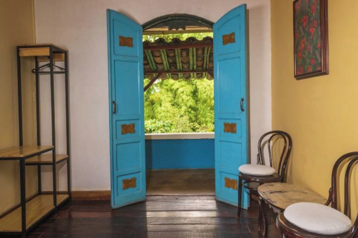An open doorway leading to a balcony with a view of greenery, wooden chairs, and a shelf unit.