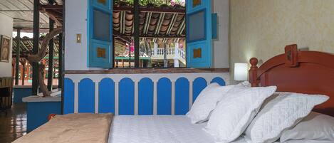 Una cama con ropa blanca, un cabecero de madera y una ventana con contraventanas azules.