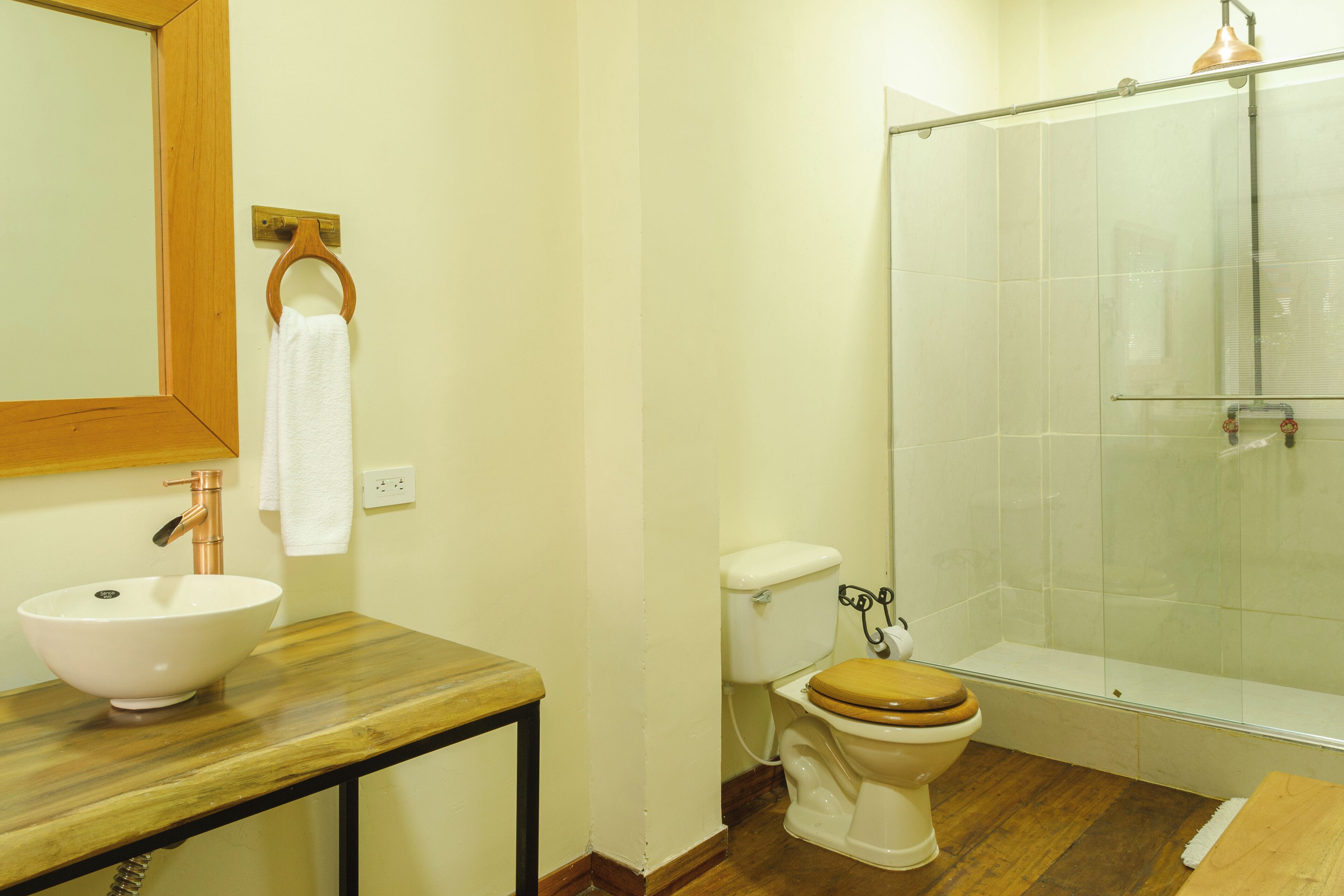 Un baño con tocador de madera, lavabo blanco, inodoro y cabina de ducha de vidrio.