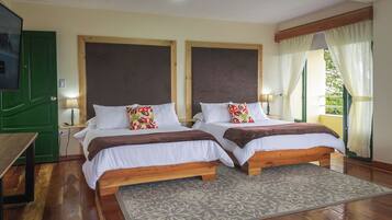 A room with two wooden beds, white bedding, patterned pillows, a wooden nightstand, a green door, and a window with curtains.