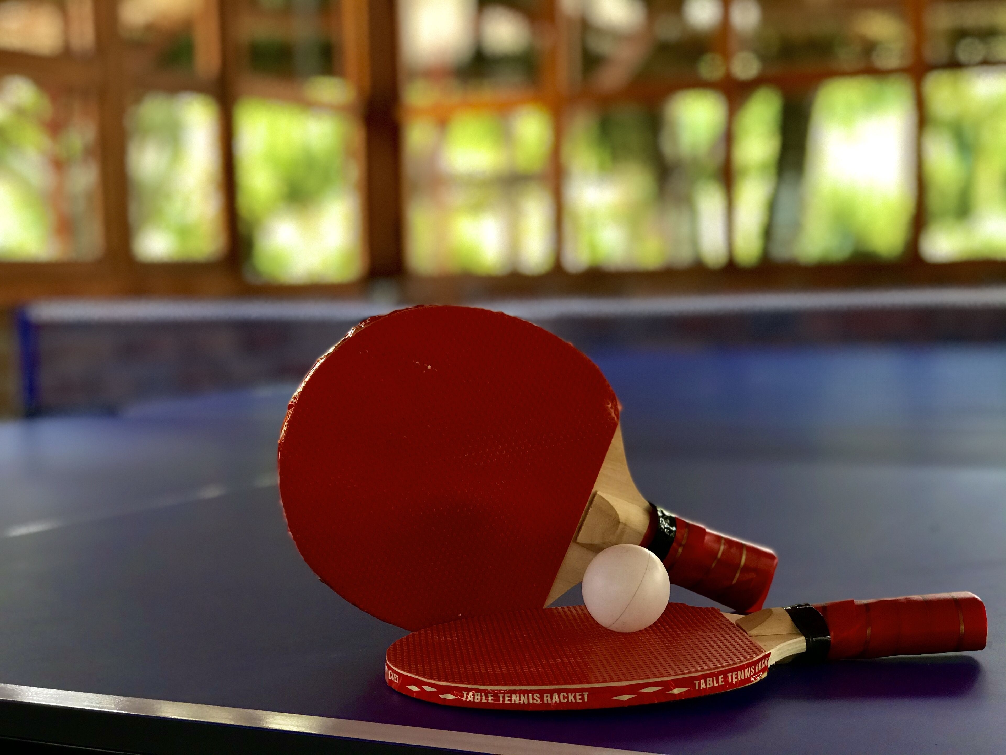 Uma mesa de tênis de mesa com uma raquete vermelha e uma bola.