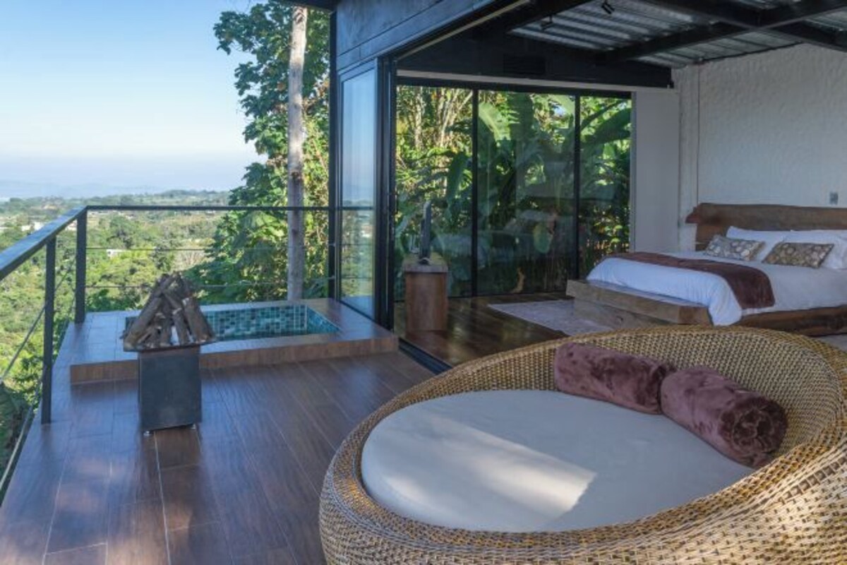 A modern bedroom with a large glass window, a bed, and a wicker chair.