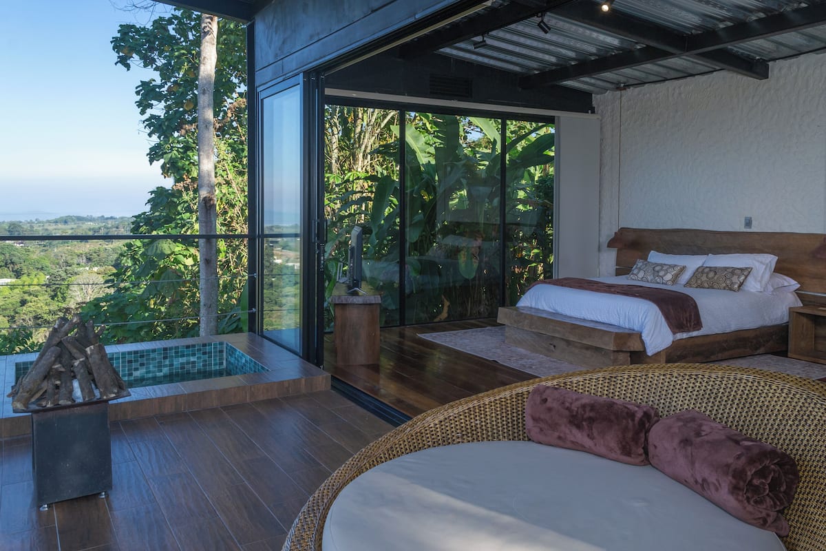 A bedroom with a large bed, a view of the outdoors, and a small pool area.