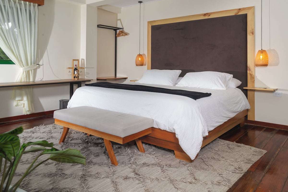 A modern bedroom with a wooden bed frame, white bedding, and a bench at the foot of the bed.