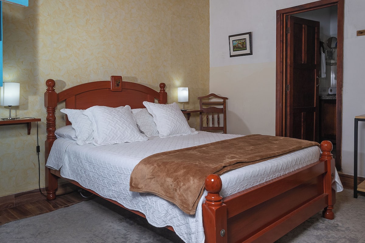 A neatly made bed with a wooden headboard, white bedding, and a brown throw blanket.
