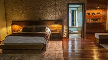 A bedroom with a wooden bed, a nightstand, a bedside table, a patterned rug, and a brick wall.