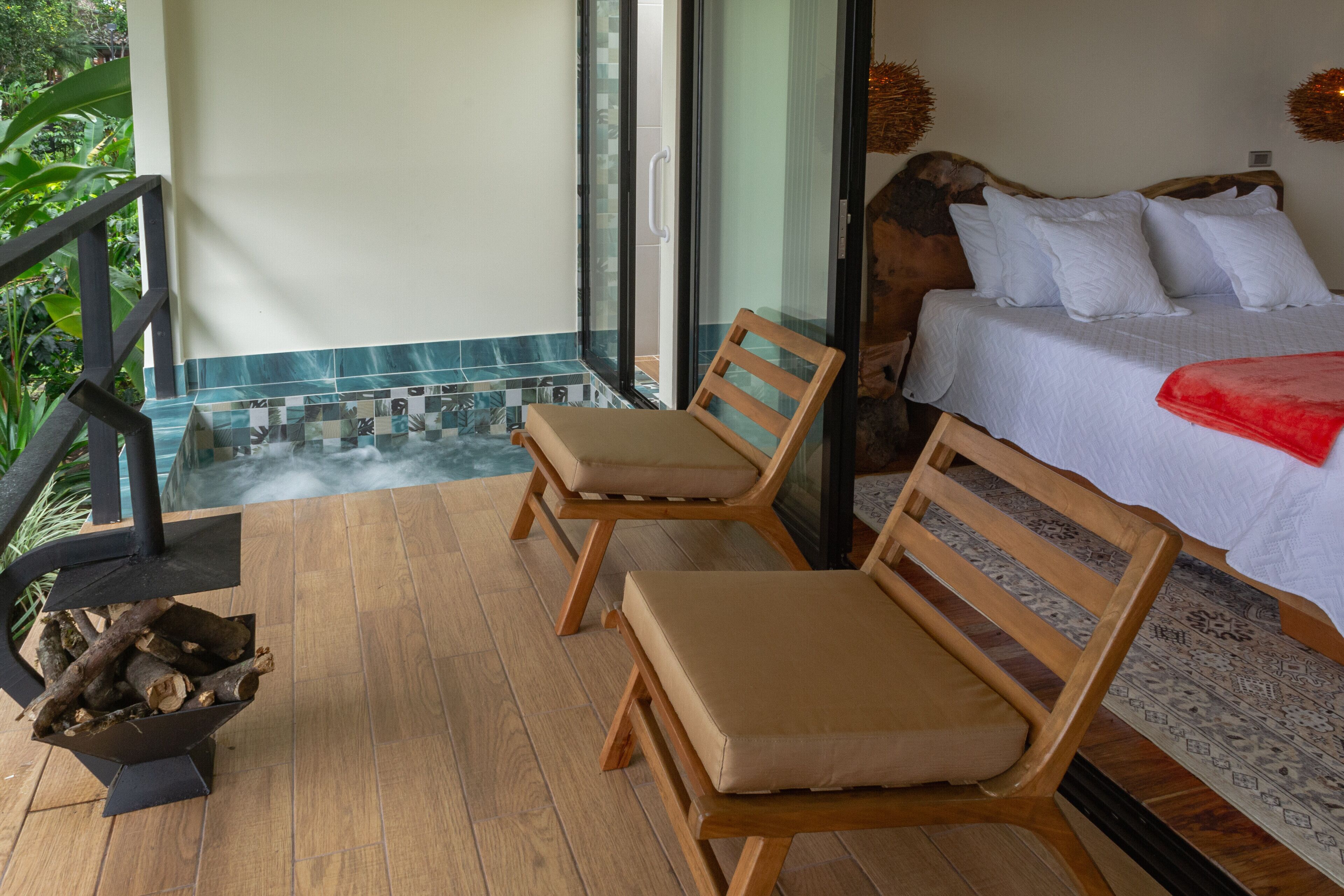 Un dormitorio con cama, dos sillas de madera, un pequeño hogar y vista a un elemento acuático.