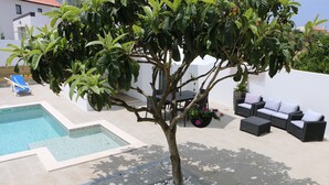 A pool area with a tree, lounge chairs, and outdoor seating. - Green house with pool (Nadadouro)