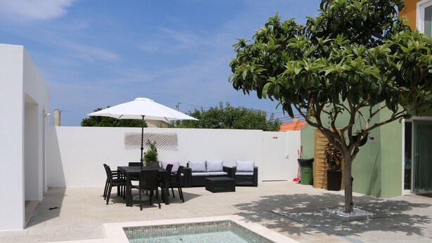 A pool area with a tiled deck, a seating area with a table and chairs, and a tree. - Green house with pool (Nadadouro)