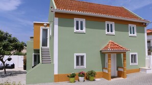 A two-story building with a green and orange facade, a tiled roof, and a small porch with potted plants. - Green house with pool (Nadadouro)