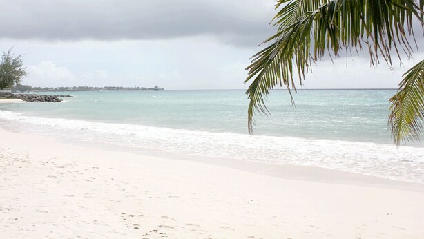 A beach with a sandy shore, calm water, and a distant ship. - Comfy 2- bedroom apartment on Barbados' South Coast, near beach and attractions! (Oistins)