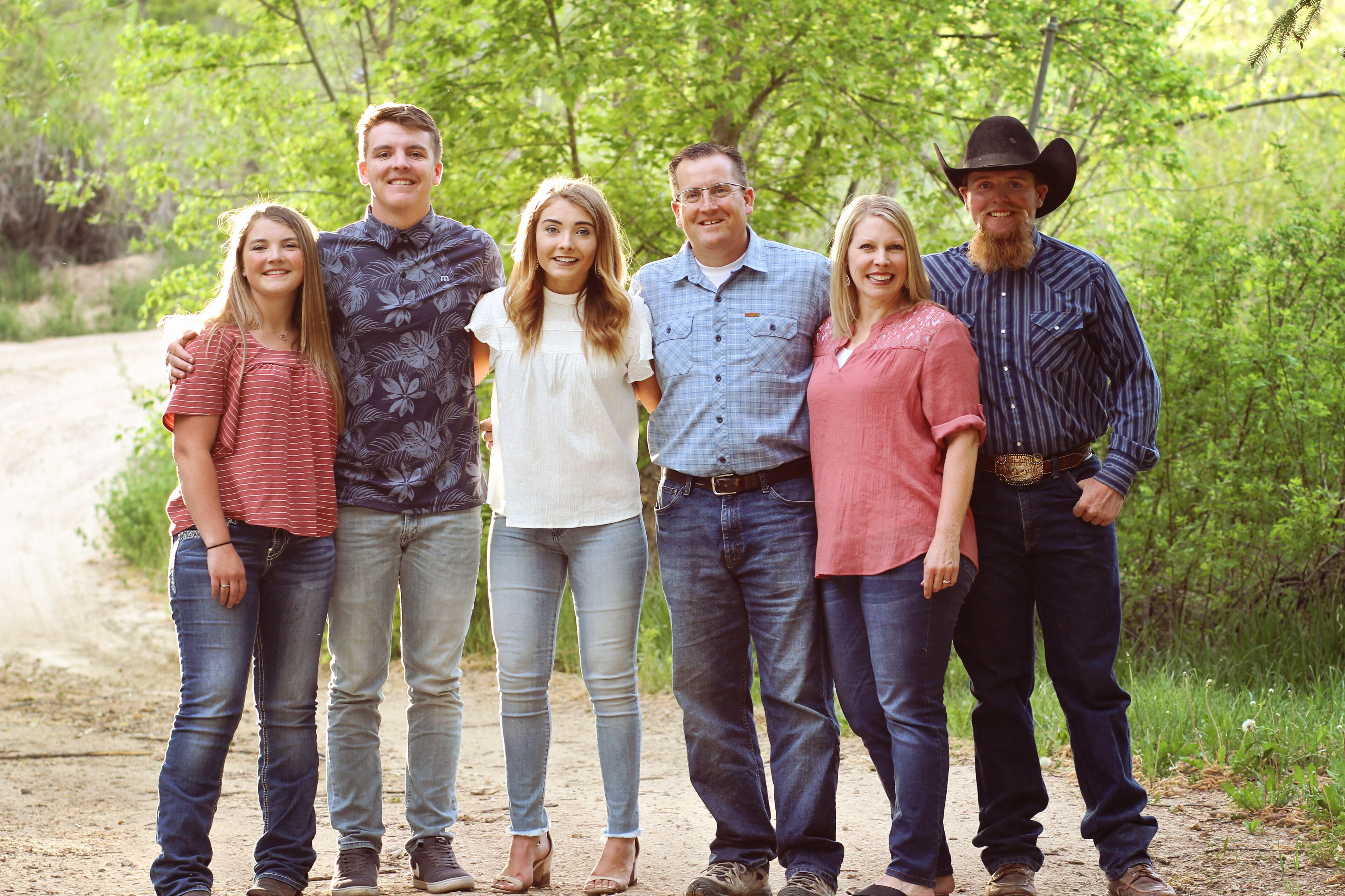 A family of six standing on a dirt path surrounded by greenery.
