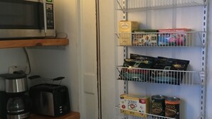 A kitchen with a microwave, toaster, and coffee maker on shelves, and a pantry with shelves holding various food items.