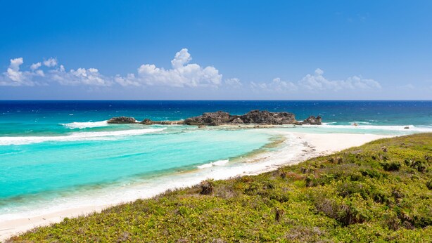 Une plage aux eaux turquoise et limpides, bordée de rochers et d’une végétation luxuriante.