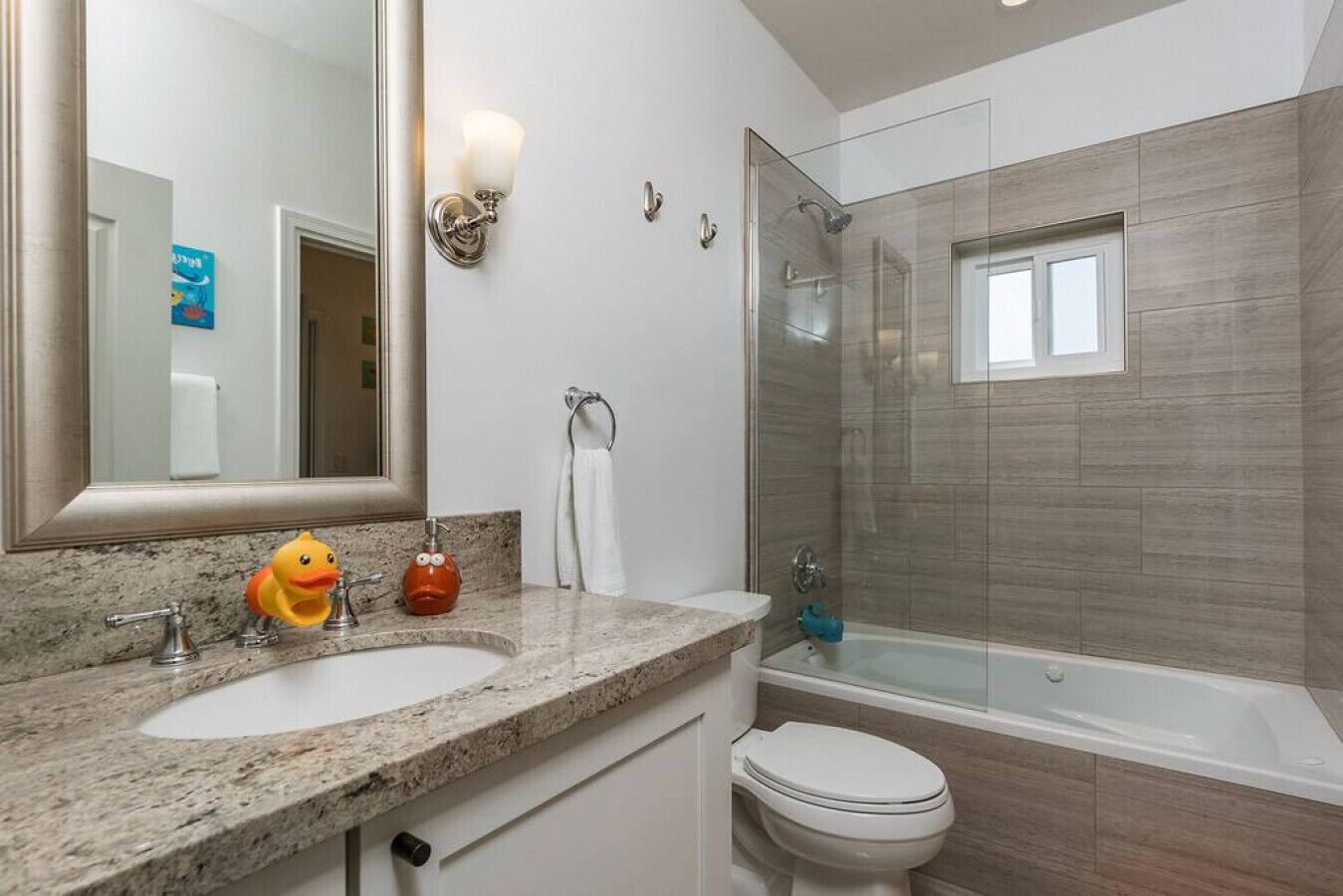 Ein modernes Badezimmer mit einer Granit-Arbeitsplatte, einem großen Spiegel, einer Toilette, einer Duschkabine und einer Badewanne.
