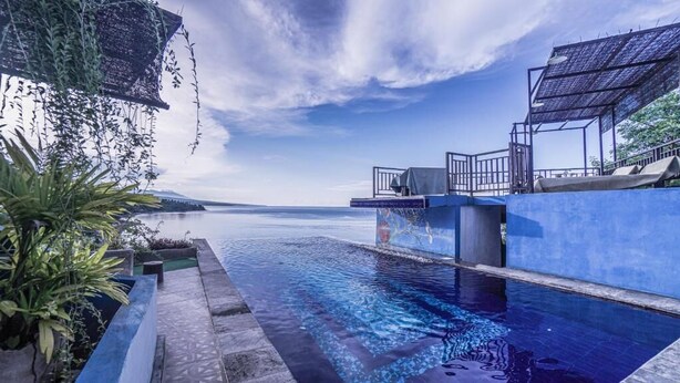 An infinity pool with a clear view of the sea, a covered seating area, and a pergola with hanging plants. - Waenis Sunset View (Karangasem)