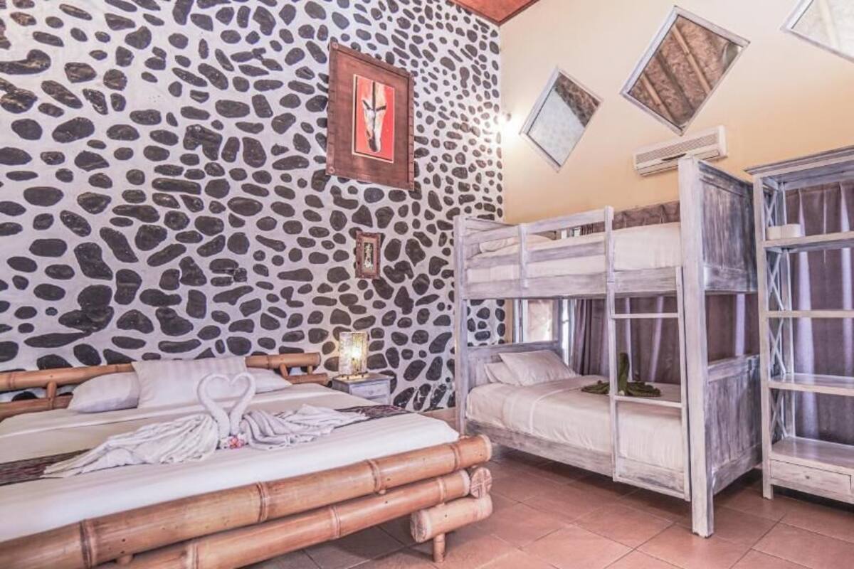 A room with a stone wall, two beds, a bunk bed, and a large window with curtains.