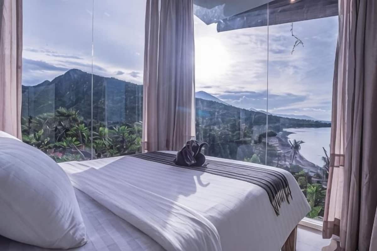 Un lit donnant sur les montagnes et un plan d’eau, grâce à de grandes fenêtres.