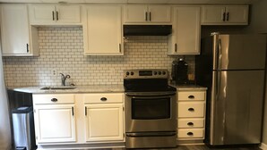A kitchen with white cabinets, a stainless steel oven, a refrigerator, and a tiled backsplash. - Tranquil Escape~Modern 1BD Suite on Greenway (Charlotte)