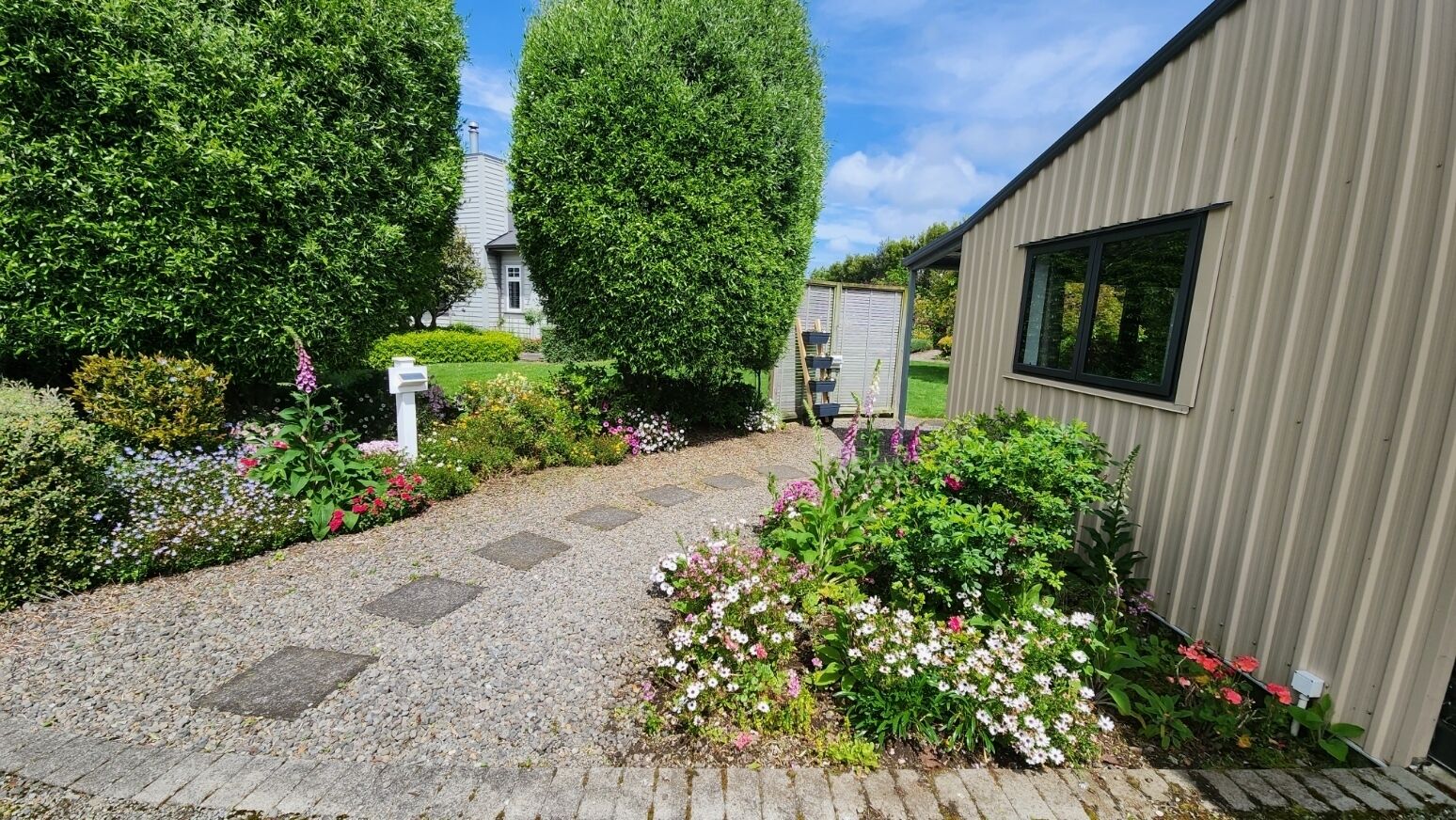 Un chemin de jardin qui mène à un bâtiment dont la façade est recouverte de tôles ondulées.
