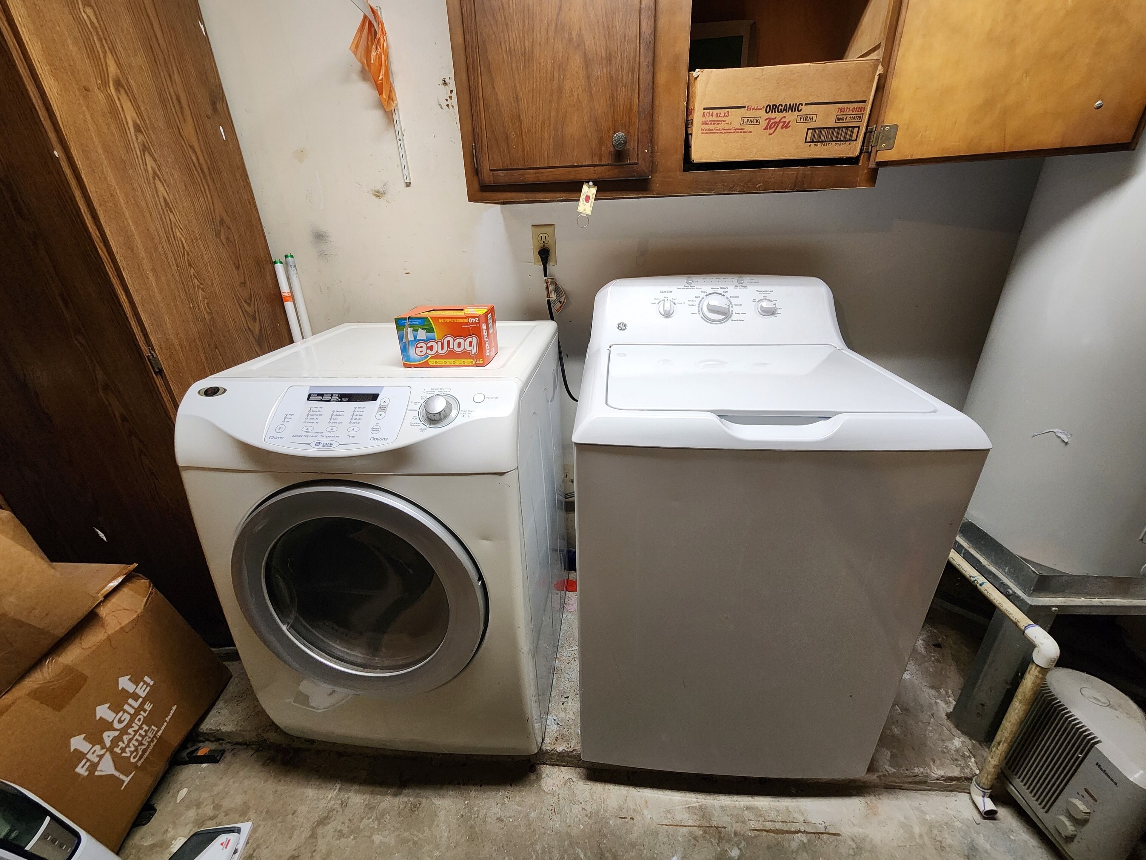 A laundry area with a front-loading washing machine and a dryer. There is a cardboard box on the dryer and a small orange umbrella hanging on the wall.